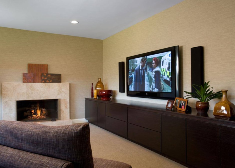 Телевизор на стене в гостиной с камином в тумбе